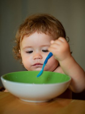 Elinde kaşıkla tabaktan yemek yiyen komik bir çocuğun portresi.
