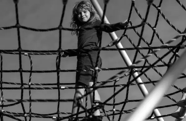 Child boy climbed on top of the rope web on playground. Child climbing the net. Kids play and climb outdoors on sunny summer day