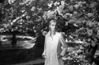 Bahar modası, pembe ceketli kız bahçede çiçek açan sakuranın tadını çıkar. Çiçekler kadınları mutlu eder. Bahar çiçeği. Şefkat ve kadınlık. Kiraz ağacı