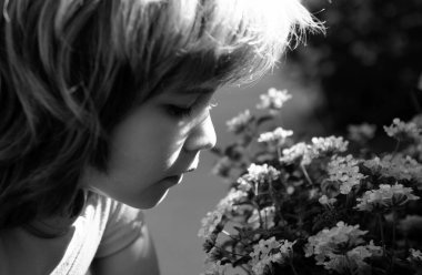 Bahar ya da yaz çocuğu çiçek açan dalı koklar. Çiçek açan bahçede tatlı bir çocuk.