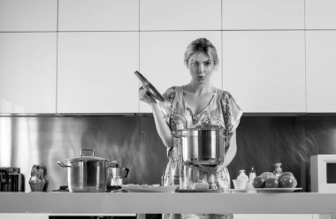 Sabahları modern mutfakta tenceresi olan bir kadın. Samimi mutfakta yemek pişiren güzel bir genç kadının portresi. Modern iç mekan, mutfak mobilyası.