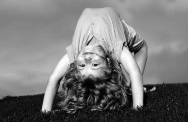 Mutlu çocuk yaz güneşinde çimlerin üzerinde amuda kalkıyor. Parktaki çimlerin üzerinde baş aşağı duran komik mutlu küçük çocuk. Çocukluk kavramı