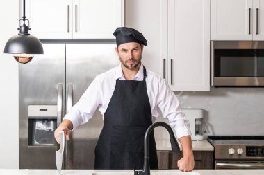Üniformalı yakışıklı aşçı mutfakta yemek yapıyor. Restoran menüsü konsepti. Fırıncı üniformalı İspanyol adam. Aşçılık ve aşçılık. İş üniformalı, siyah önlüklü, şef şapkalı bir aşçı.