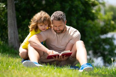 Baba ve oğul parkta kitap okuyor. Eğitim ve arkadaşlık kavramı. Hayat tarzı, babası sevimli oğluna bir kitap okumuş. Sıcak bir yaz günü, aile ilişkisi, çocuk ve ebeveyn, bekar.