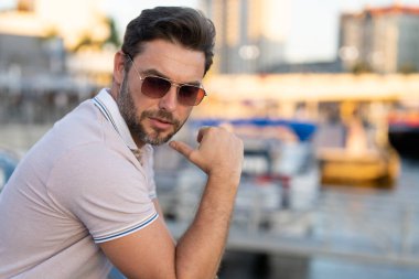 Sokakta polo tişörtlü yakışıklı bir genç. Dışarıda poz veren yakışıklı, kendine güvenen bir hippi modeli. Amerikan şehrinin arka planında seksi moda erkeği