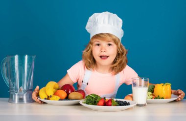 Aşçı önlüğü giymiş çocuk aşçı ve stüdyo arka planında izole edilmiş şef şapkası. Sağlıklı beslenme çocuklar için.