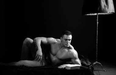 Seksi vücut geliştirme atleti, çıplak gövdesiyle lüks bir iç mekanda yatar.