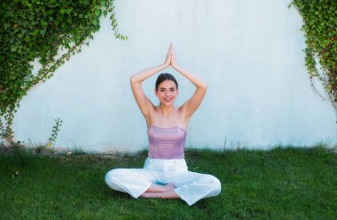 Meditation yoga woman in spring park. Woman doing stretching up exercise outdoors on green grass. Fit girl in sportswear doing morning yoga