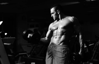 Üstsüz, güçlü vücut geliştirici, spor salonunda kol kasları çalıştırıyor. Dambıl egzersizleri. Gövdesiz sporcu. Sportif egzersiz. Atletik vücut