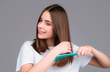 Saçını tarayan, gülümseyen güzel bir genç kadının portresi. Tarakla sağlıklı saç tarayan bir kadın.