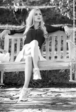 Young woman swinging on a swing in park. Beautiful woman relaxing at a swing in garden. Summer fashion portrait of sensual girl