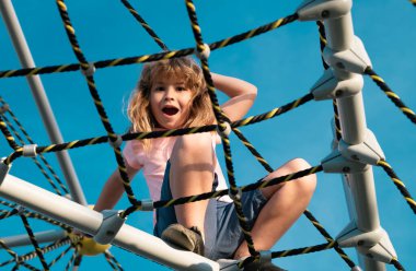 Çocuklar güneşli yaz gününde dışarıda oynar ve tırmanırlar. Çocuk çocuk oyun parkındaki halat ağına tırmandı. Çocuk ağa tırmanıyor.