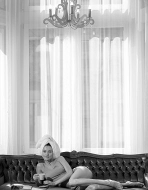 Lüks yatak odasındaki rahat bir kanepede dinlenen ve uzanan bir kız. Çekici seksi kadın otelde bornoz ve havlu giyerek rahatlıyor.