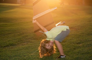 Beyaz çocuk, çimenli yaz tepesinin dışında, güneşli, altın renkli gökyüzü arka planında oyuncak uçakla oynuyor. Mutlu gelecek konseptini hayal ediyorum. Çocukların yüz ifadesi