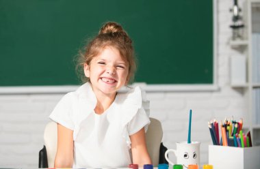Cute little preschooler child girl drawing at school. Child girl painting on elementary school. Funny school girl face