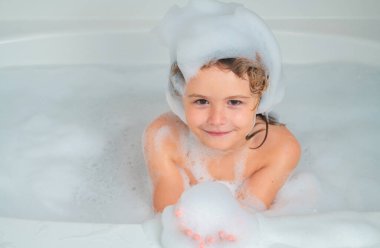 Yüzü köpüklü çocuklar gibi. Çocuk banyo köpüğüyle yıkanıyor. Tatlı çocuk banyo yapar, beyaz bir banyoda sabun köpüğü ve şampuanla yatar.