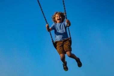 Zincirle sallanan küçük çocuk şehir çocuklarının oyun alanında sallanıyor. Sallanma turu. Salıncakta salıncakta sallanan tatlı bir çocuk. Sarışın küçük çocuk çocuk parkında sallanıyor. Yüksekten sallanan çocuk