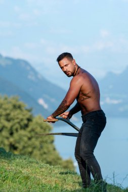 Tırpan kullanan bir adam. Yeşil çim tarlasında tırpanlı bir çiftçi. Adam çim biçmiş. Kır çiftçisi yaz çayırında geleneksel tırpanla çim biçiyor.