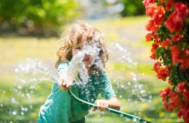 Çocuklar bahçede su hortumuyla oynuyorlar. Açık hava çocukları yaz eğlencesi. Küçük çocuk arka bahçede su hortumuyla oynuyor. Çocuklar için parti oyunu. Sıcak güneşli bir gün için sağlıklı aktivite