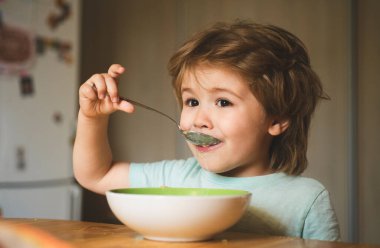 Bebek maması. Çocuk için yiyecek ve içecek. Mutfakta masada yemek yiyen çocuk. Mutlu erkek bebek sağlıklı yemek kaşığı yiyor.