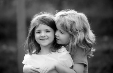 Yaz günü dışarıda sevimli mutlu çocuklar, küçük bir çocuk bir kızı öpüyor. Sevimli küçük kız ve oğlan, dışarıda eğlenin ve sarılın. Komik çocuk suratı