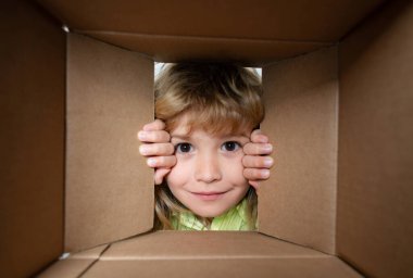 Child open paper cardboard box. Kid boy unpacking and opening carton box looking inside with surprise face. Parcels and delivery