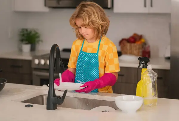 掃除屋だ 子供の男の子は台所の流しで皿を洗う 洗剤とクリーニングアクセサリー 清掃サービス 小さな男の子のハウスキーピング — ストック写真