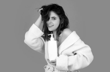 Stüdyoda ıslak saçlı güzel bir genç kız. Güzellik kremi kozmetik ürünleri. Kadın şişe şampuanı ve saç kremi tutuyor.