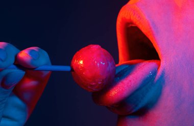 Kadın ağzında lolipop, kırmızı ruj. Kırmızı, parlak bir lolipopu yalayan bir kadın. Kapatın. Neon ışıklarda seksi ağızda lolipopu olan seksi bir kadın. Gece kulübü geçmişi