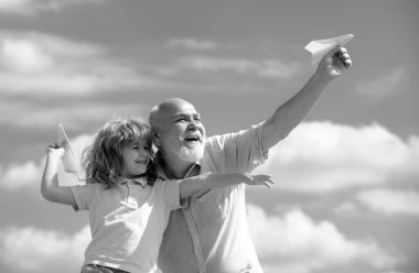 Yaşlı büyükbaba ve küçük torun ve oyuncak kağıt uçakla yaz gökyüzü arka planına karşı. Uçma hayali kuran çocuk