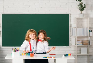 Sınıfta karatahta arka planda komik öğrenciler çiziyor. Okul arkadaşları çocuklar, kız ve erkek birlikte resim yapıyorlar. Çocukların yaratıcı gelişimi