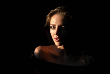 Stüdyoda poz veren genç bir kadın. Işık ve gölge. Yüzünde koyu renk ışık olan güzel bir kadının moda portresi. Şehvetli baştan çıkarıcı kadının yüzüne çarpıcı bir ışık.