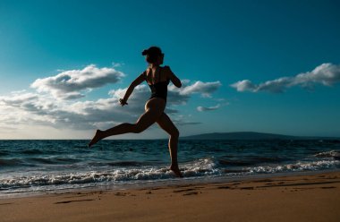 Sağlık ve zindelik için okyanus kıyısında sörf yapan bir kadın. Yaz tatilinde kadın fitness, koşu ve spor aktiviteleri.
