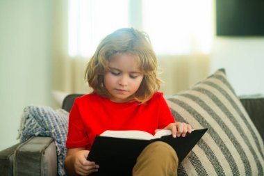 Eğitim kavramı, çocukluk, kitap okuma, sanat eseri, ilham. Evde kitap okuyan bir çocuk. Küçük çocuk oturma odasında kanepede oturmuş masal kitabı okuyor. Çocuk okul için ödev yapıyor.