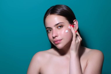 Yüzüne krem süren genç bir kadın. Cilt bakımı ve kozmetik konsepti. Cilt bakımı. Stüdyo geçmişine krem süren bir kız. Cilt nemlendirici