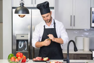 Yakışıklı adam mutfakta yemek hazırlıyor. Yakışıklı, orta yaşlı bir adam mutfakta et pişiriyor. Adam mutfakta yemek hazırlıyor. Mutfak konseptinde sağlıklı yemek ve yemek.