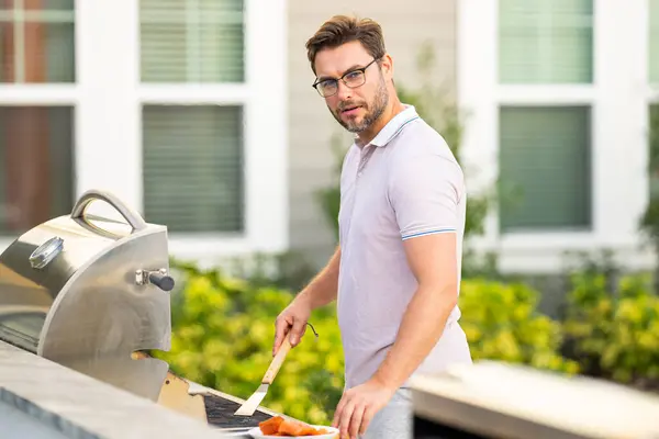 Handsome man preparing barbecue grill outdoor. Man cooking tasty food on barbecue grill at backyard. Chef preparing food on barbecue. Millennial man grilling meat on grill. Bbq party. Meal grilling