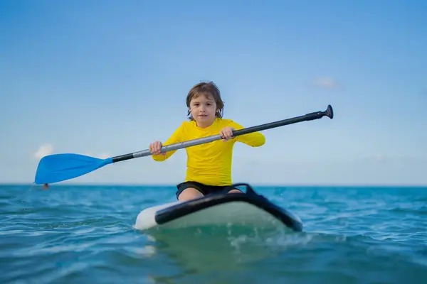 Kid swimming on stand up paddle board. Water sports, active lifestyle. Kid paddling on a paddleboard in the ocean. Child Paddle boarder. Summer Water sport, SUP surfing. Summer beach vacation