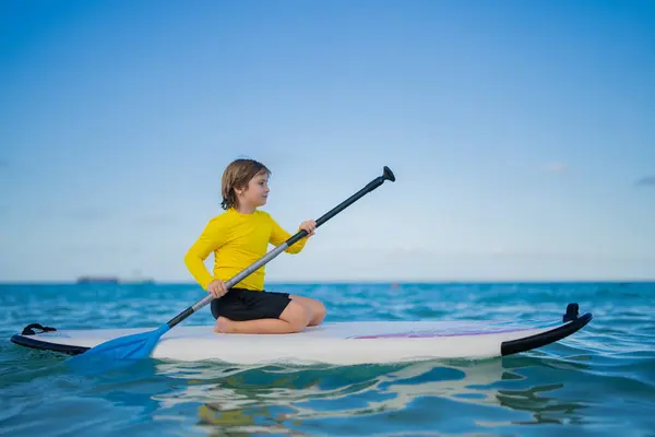 stock image Kid swimming on stand up paddle board. Water sports, active lifestyle. Kid paddling on a paddleboard in the ocean. Child Paddle boarder. Summer Water sport, SUP surfing. Summer beach vacation