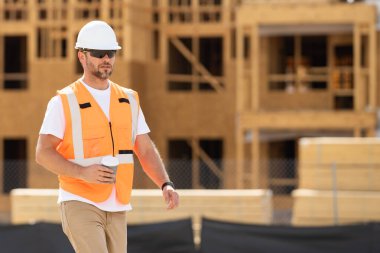 Amerikan ahşap bina inşaatında kahve molası vermiş miğferli bir inşaatçı. Yeni bir ev inşa etmeye hazır müteahhit portresi. İnşaat alanında kasketli işçi.