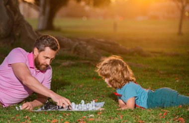 Baba ve oğul dışarıda satranç oynuyorlar. Genç çocuk satrançta bir adamı yeniyor.