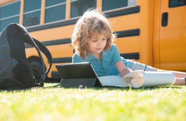 Okul otobüsünün yanındaki parkta çimlerin üzerinde yatan sevimli okul çocuğu. Okul çocuğu dışarıda.
