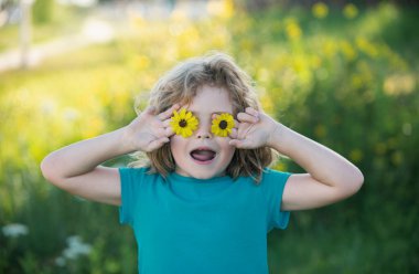 Gözlerinin önünde çiçek tutan komik bir çocuğun portresi. Kafkas çocuk yüzünü kapatın. Komik çocuğun yakın plan kafası.