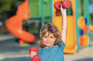 Yaz sporu, çocuklar oyun alanında spor eğitimi. Kol kaslarını halterle şişiren sevimli çocuk. Dambılı spor çocukları.