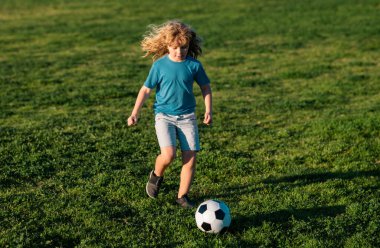 Futbolcu. Çocuklar yaz stadyum sahasında futbol oynarlar. Küçük çocuk topa vuruyor. Küçük çocuk kaleye ateş ediyor, çocuk futbol topunu tekmeliyor