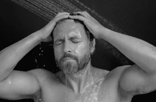 Man washing hair in bath. Guy bathing shower head in bathtub. Face in foam in shower. Bathing man taking shower. Close up guy showering. Shower concept. Man is under water drops in showers