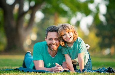 Baba ve oğul yazın gülümsüyor. Parkta arka plan bulanıklaşıyor.