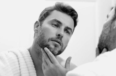 Yüz kremi süren güzel bir adamın güzel yüz portresi. İnsan için nemlendirici cilt kremi. Maske, deri değiştirme ve yaşlanmayı önleyici etki. Güzel erkek yüzü konsepti. Cilt bakımı ve yaşlanma. Yüz Kozmetiği