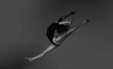 Bacak bacak sıçraması. Siyah arka planda esnek seksi kadın vücudu. Seksi kadın egzersizi. Vücut giysisi içinde zayıf seksi bir kadın vücudu. Seksi kadın poz esneme hareketleriyle esniyor. Formda sporcu geriliyor