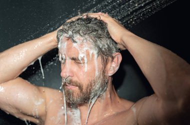 Saç yıkayan bir adam, yakın plan bir portre. Banyoda duş alırken saçlarını yıkarken. Erkek model duşta saç yıkıyor. Adam duş alıyor. Duş alan adam, saç bakımı. Erkek şampuanı ve saç yıkama konsepti